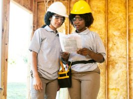 2 women in hard hats reviewing paperwork within construction site; frame up, walls with insulation visible