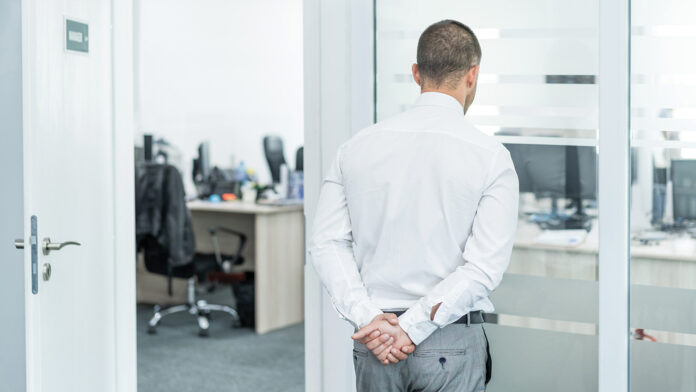 Worried businessman with his hands behind his back, watching the empty office,during COVID-19 Tough Call the Peter Principle