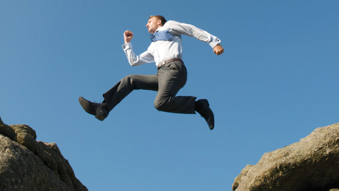 Businessman Leaps Between Big Boulders Tough call to buy or not to buy
